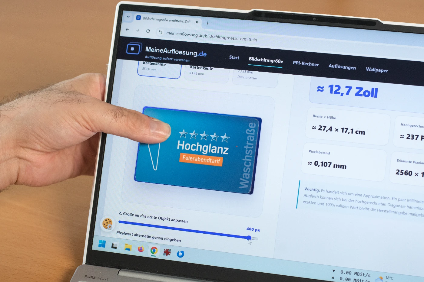 Hand hält eine Karte vor einen Laptopbildschirm mit geöffneter Seite zur Bildschirmgrößen-Ermittlung als Referenzabgleich.